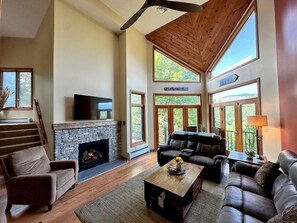 A spacious living room with a stone fireplace, leather sofas, and a large window offering a view of the outdoors.