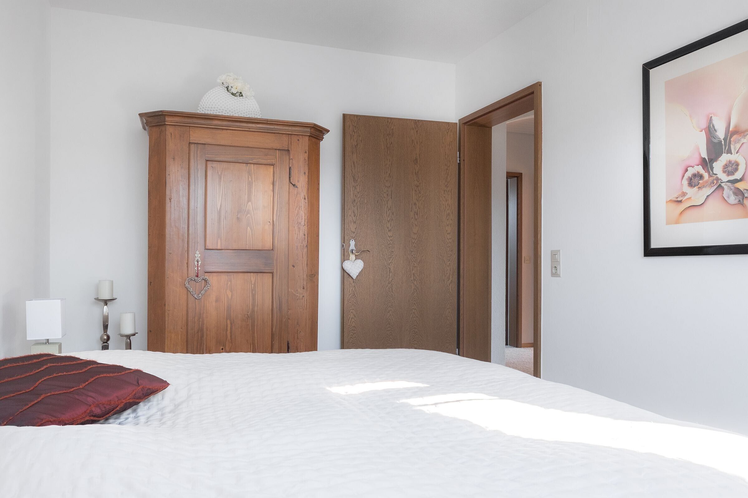 Ein Schlafzimmer mit einem Bett, einem Holzschrank, einer Tür, einem Wandbild und Nachttischlampen.