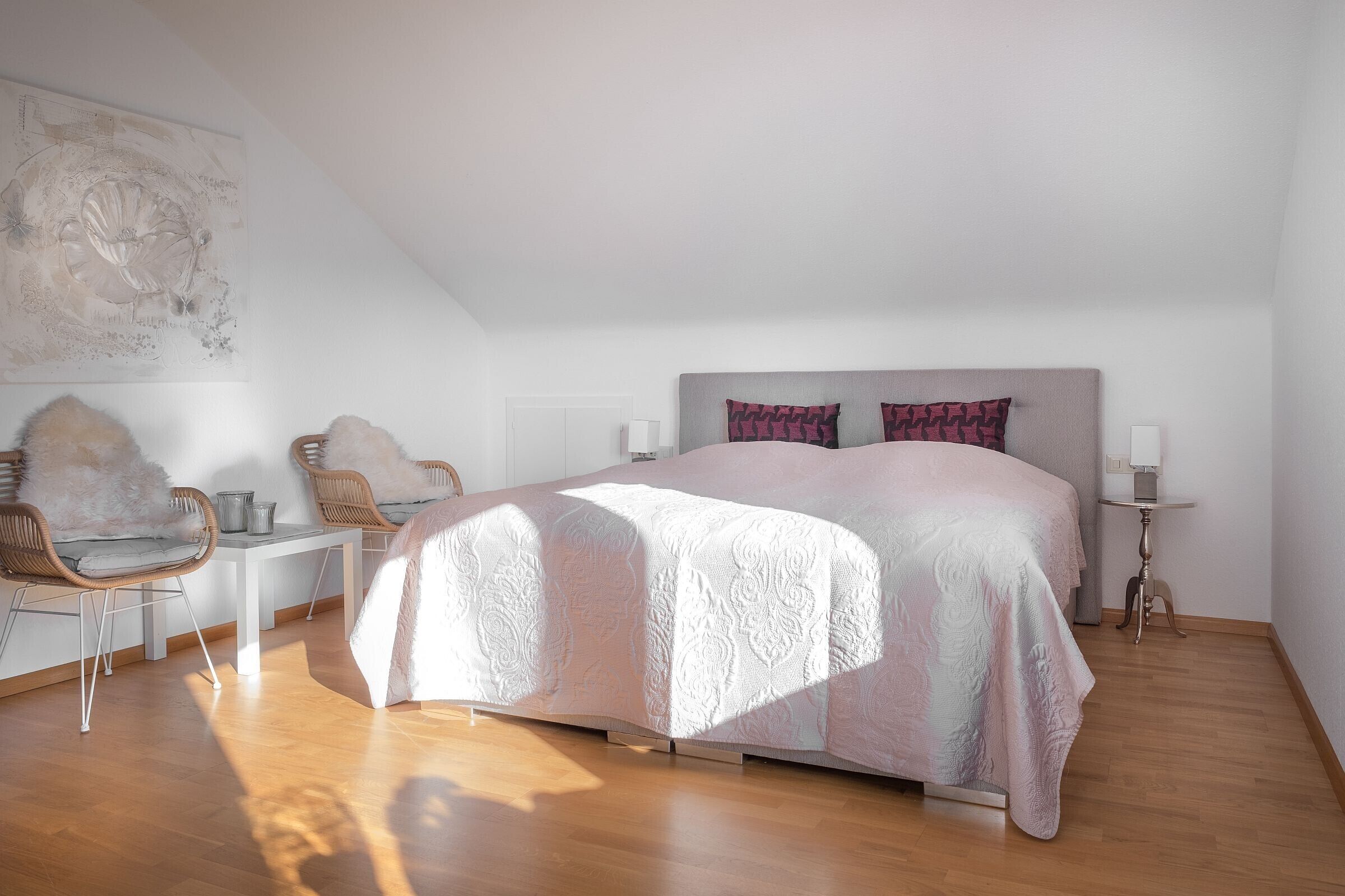 Ein Schlafzimmer mit einem Bett, zwei Stühlen, einem kleinen Tisch und einem Wandbild.