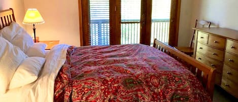 A bedroom with a bed, a nightstand, a lamp, a dresser, and a window with blinds.