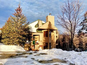 Ein zweistöckiges Haus mit einem markanten Schornstein, einer kleinen Veranda und einem schneebedeckten Garten.