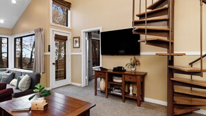 A spacious living room with a wooden staircase, a flat-screen TV mounted on the wall, and a comfortable seating area with a sofa and coffee table. - Dobie 21 With Wintergreen Advantage (Wintergreen)