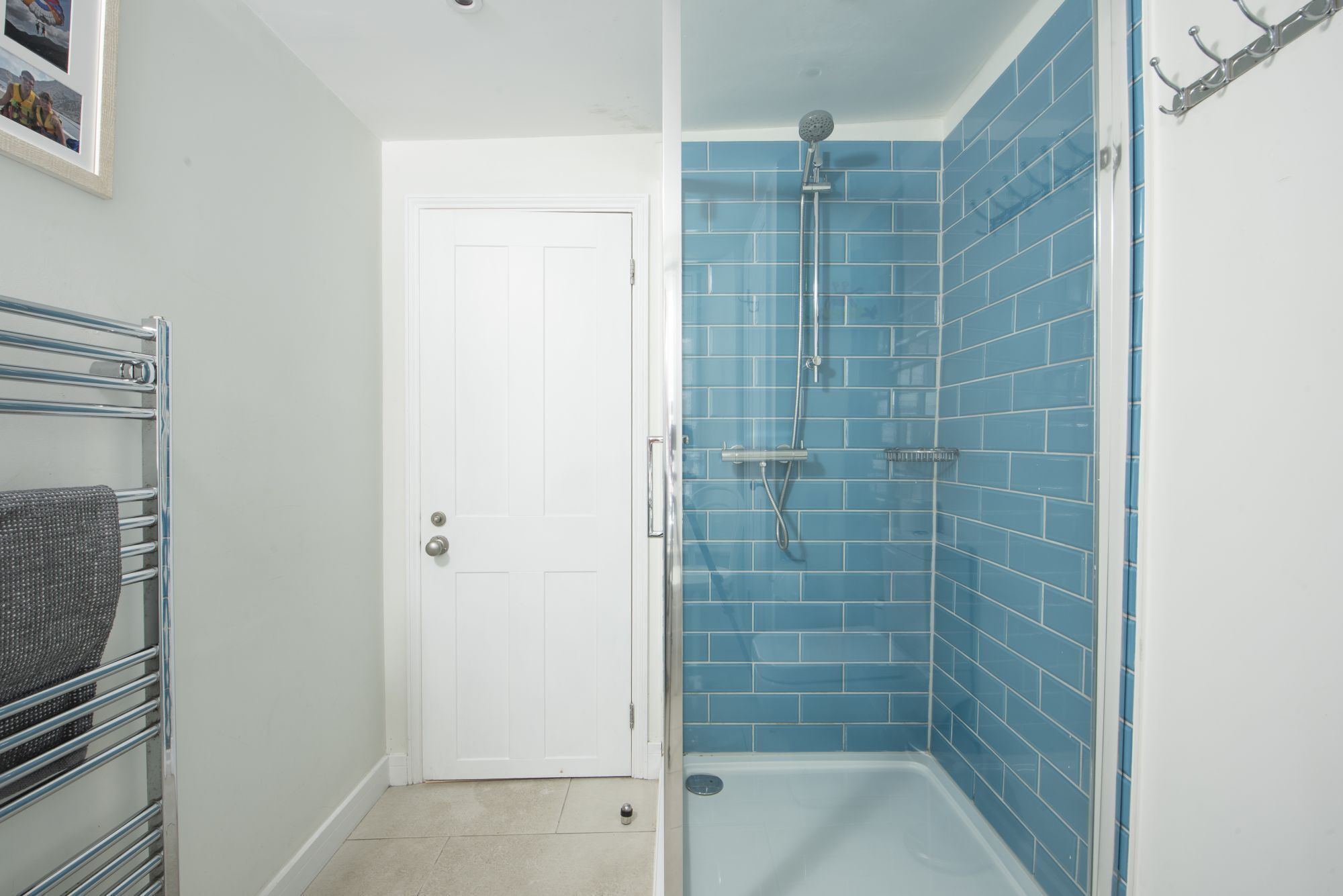 Une salle de bain avec une porte blanche, une douche aux carreaux bleus et un porte-serviettes avec une serviette grise.