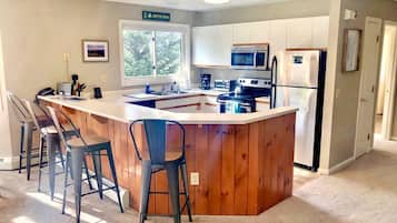 A modern kitchen with a central island, bar stools, a microwave, a refrigerator, and a window providing natural light.