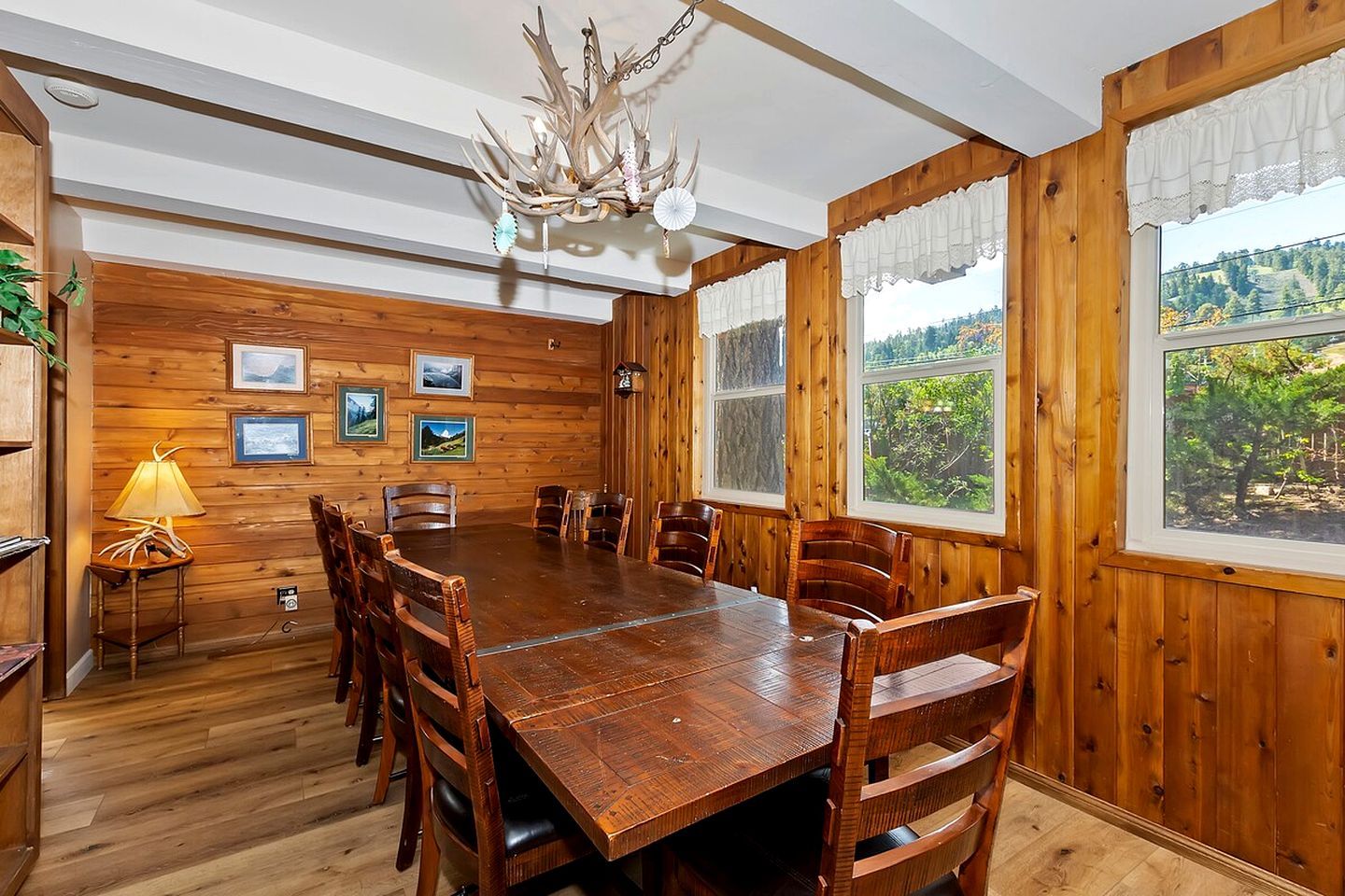 A wooden-paneled dining room with a large table and chairs, framed pictures on the wall, and a chandelier.