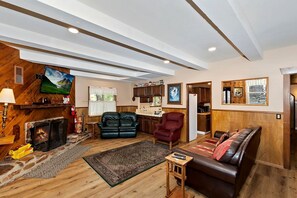 A cozy living room with a fireplace, leather sofas, a television, and a kitchen area. - Cozy Cabin with Sauna, Barbecue and Fireplace in Big Bear Lake, California (Big Bear Lake)
