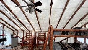 A tent-style room with a bunk bed, a desk, chairs, a refrigerator, and a ceiling fan.