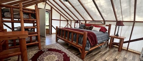 Alojamiento con tienda de campaña, cama de madera, alfombra roja y ventilador de techo.