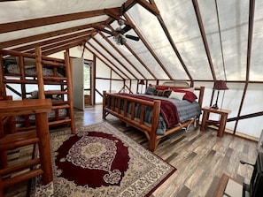 Alojamiento con tienda de campaña, cama de madera, alfombra roja y ventilador de techo.