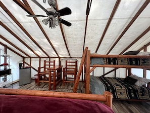 Una habitación tipo tienda de campaña con literas, un escritorio, sillas, un refrigerador y un ventilador de techo.