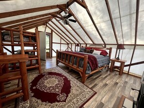 Alojamiento con tienda de campaña, cama de madera, alfombra roja y ventilador de techo.