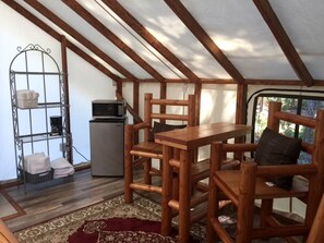 Una carpa con una mesa y sillas de madera, un estante metálico y un refrigerador pequeño.