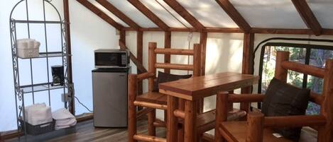A tent with a wooden table and chairs, a metal shelf, and a small refrigerator.