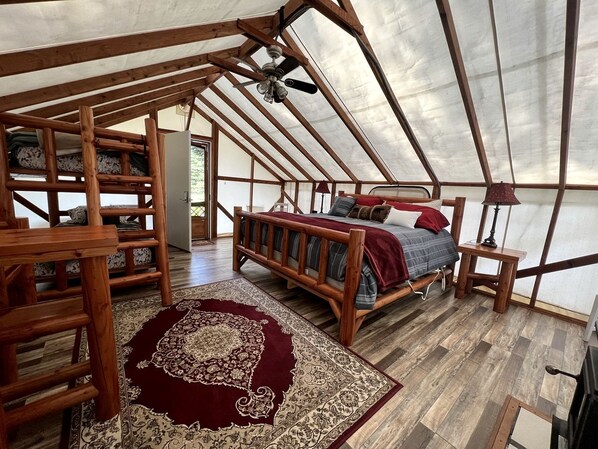 A tented accommodation with a wooden bed, a red rug, and a ceiling fan.
