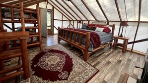 A tented accommodation with a wooden bed, a red rug, and a ceiling fan.