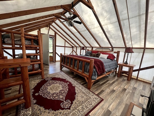 Un hébergement sous tente comprenant un lit en bois, un tapis rouge et un ventilateur de plafond.