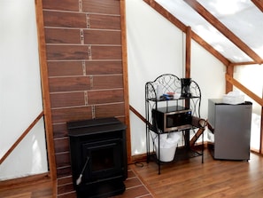Una habitación con estufa de leña, repisa metálica con objetos y un refrigerador.