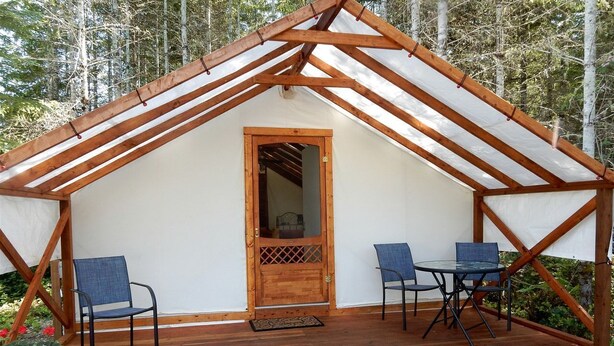 Une structure en bois dotée d’un toit à deux versants, d’une porte et de deux tables accompagnées de chaises.