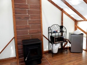 A room with a wood-burning stove, a metal shelf with items, and a refrigerator.