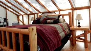 Une chambre à coucher avec un lit en bois, une couverture rouge, des coussins à motifs, une table de chevet et une lampe.