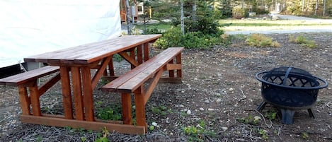 A wooden picnic table and a black fire pit in a natural setting.
