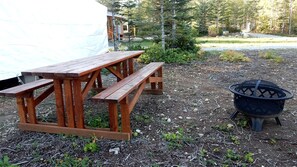 Une table de pique-nique en bois et un foyer noir, le tout dans un cadre naturel.
