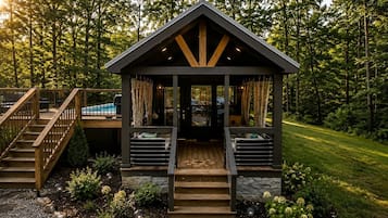 A wooden cabin with a porch, stone steps, and a view of a swimming pool.