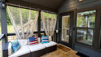 A covered porch with a seating area featuring a sofa and cushions, a hammock, and a door with a window.