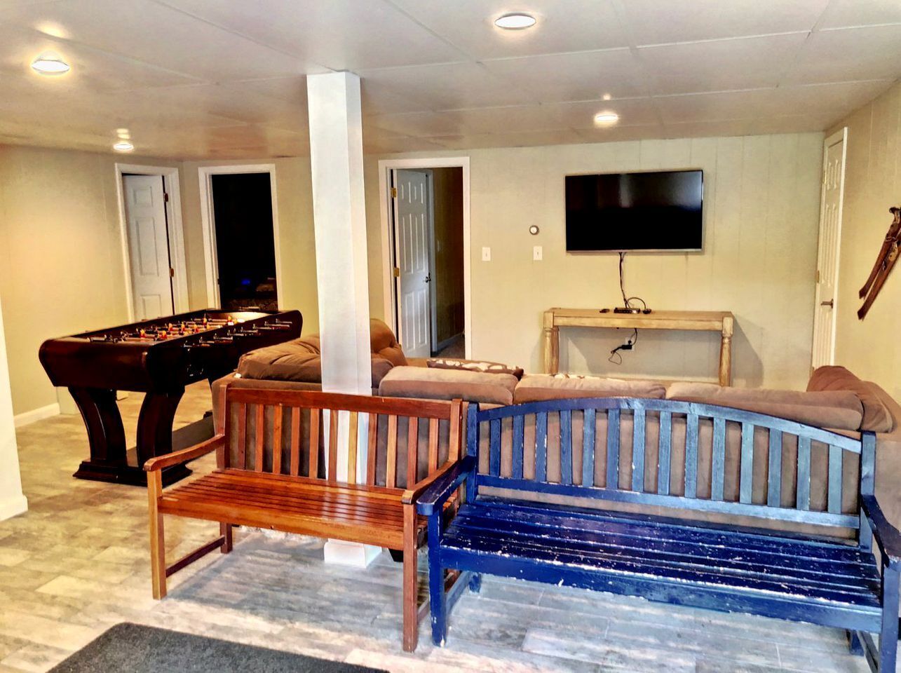 A living room with a foosball table, a blue and brown bench, a TV on the wall, and a piano.