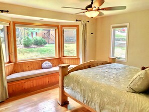 Un dormitorio con cama, asiento junto a la ventana y ventilador de techo.