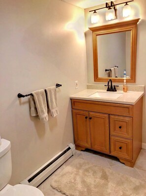 Un baño con inodoro, lavamanos, tocador, espejo, toallero y piso con calefacción.