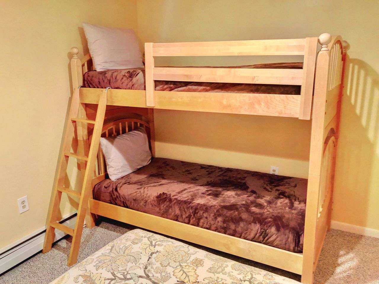 A bunk bed with a ladder, a pillow, and a patterned rug.