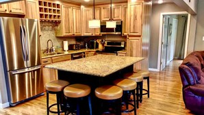 A kitchen with a central island, bar stools, stainless steel appliances, wooden cabinets, and a wooden floor. - Slopeside Bretton Woods Resort Cottage for Families (Carroll)