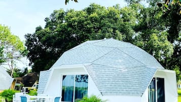 A dome-shaped building with a white exterior and large windows, surrounded by greenery.