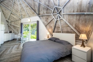 A bedroom with a sloped ceiling, a bed, a nightstand, a lamp, a chair, and a view of the outdoors.