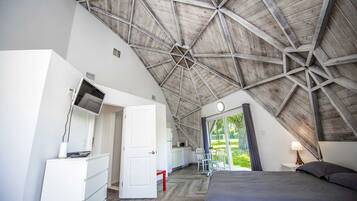 A bedroom with a sloped ceiling, a bed, a desk, a chair, and a window.