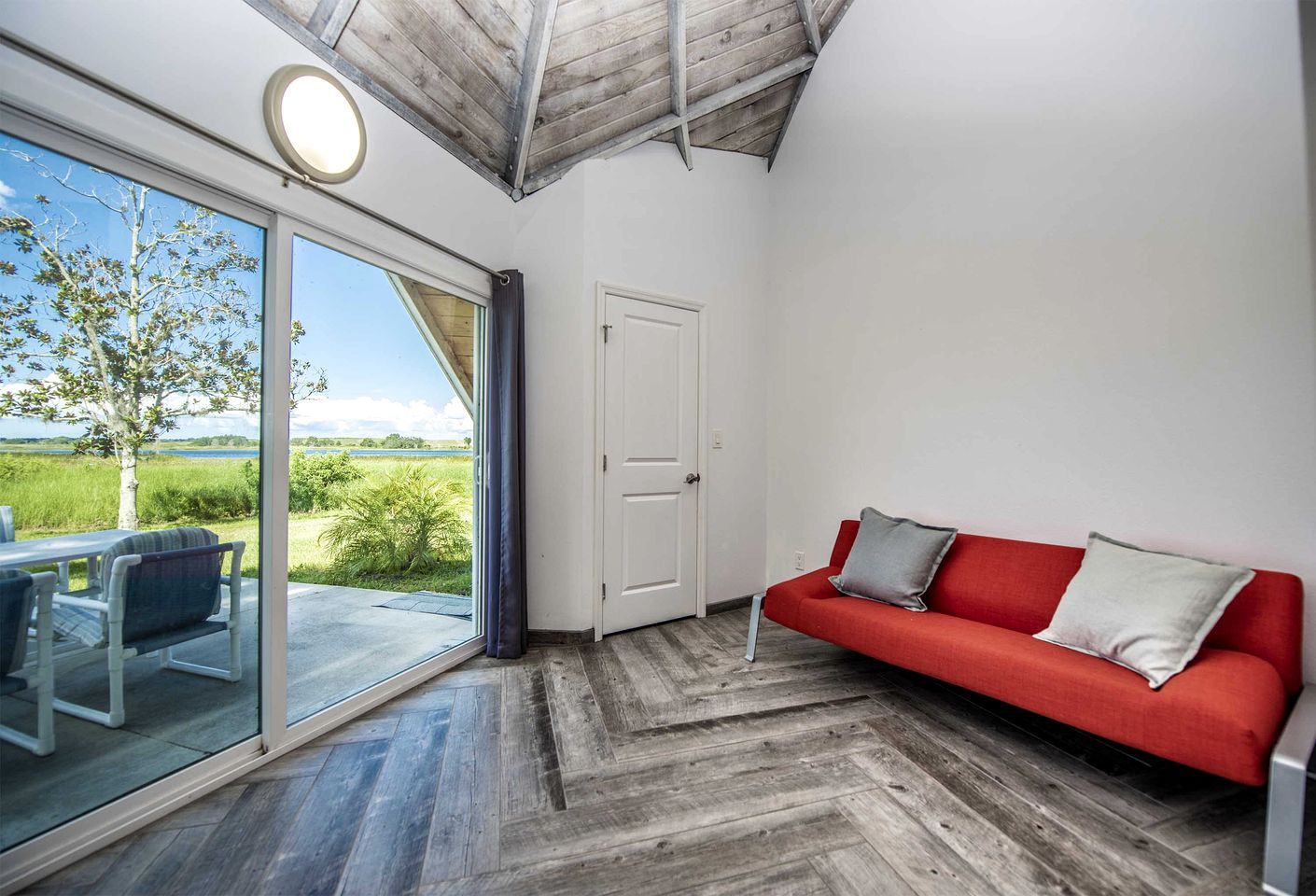 A room with a red sofa, a glass door leading to an outdoor area, and a herringbone wooden floor.