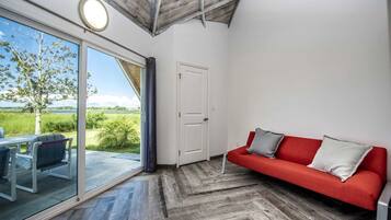A room with a red sofa, a glass door leading to an outdoor area, and a herringbone wooden floor.