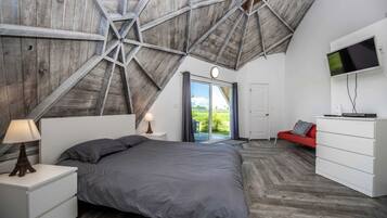A bedroom with a sloped ceiling, a bed, a TV, a dresser, and a red sofa.