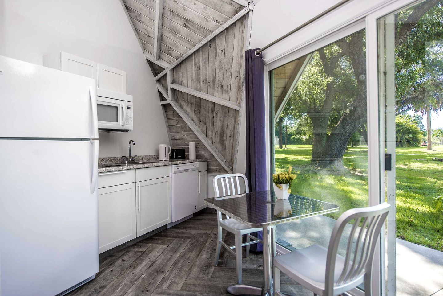 A compact kitchen with white cabinets, a microwave, and a dining area with a glass table and chairs.