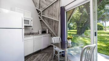 A compact kitchen with white cabinets, a microwave, and a dining area with a glass table and chairs.