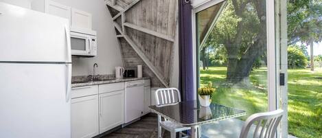 A compact kitchen with white cabinets, a microwave, and a dining area with a glass table and chairs.