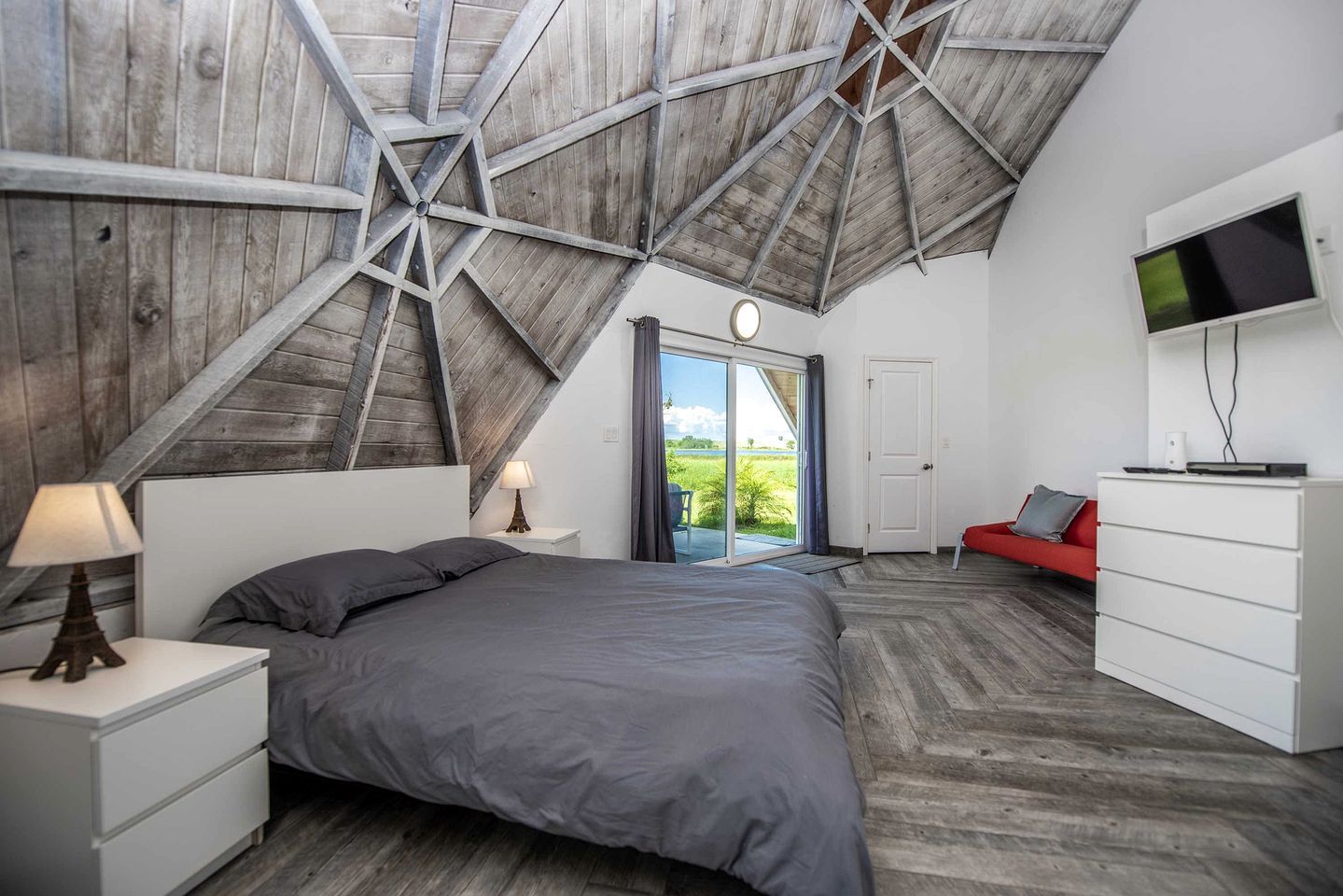 A bedroom with a sloped ceiling, a bed, a TV, a dresser, and a red sofa.