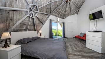 A bedroom with a sloped ceiling, a bed, a TV, a dresser, and a red sofa.