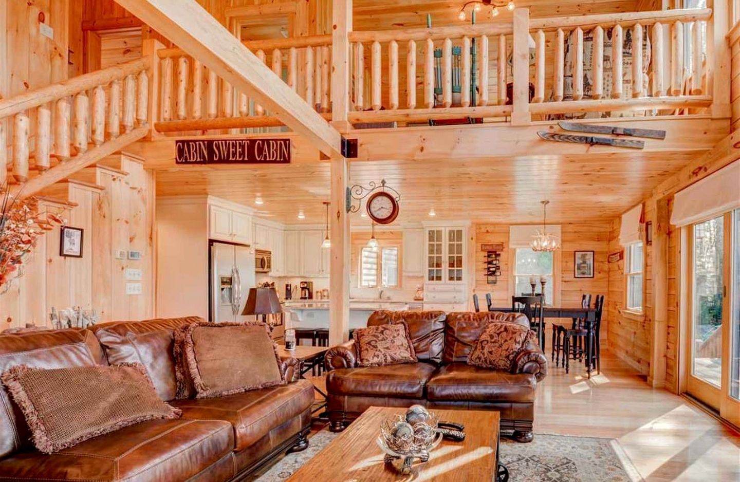 A cabin interior with a living area, dining space, and a staircase leading to a loft.