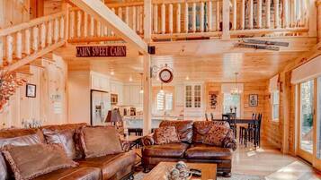 A cabin interior with a living area, dining space, and a staircase leading to a loft.