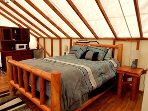 Ein hölzernes Bett mit gemusterten Betttextilien in einem Raum mit schrägem Dach und Holzbalken.