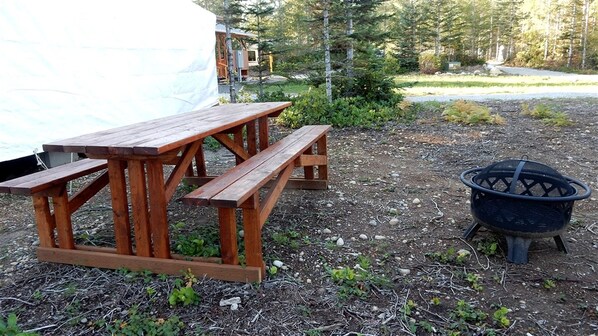 A wooden picnic table and a black fire pit in a natural setting.
