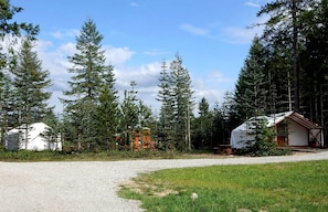 Ein Kiesweg führt zu einer Reihe von Holzhütten, umgeben von dichtem Wald.