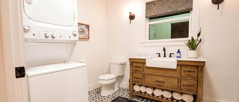 A bathroom with a washing machine, toilet, vanity with a sink, and a window with a view.